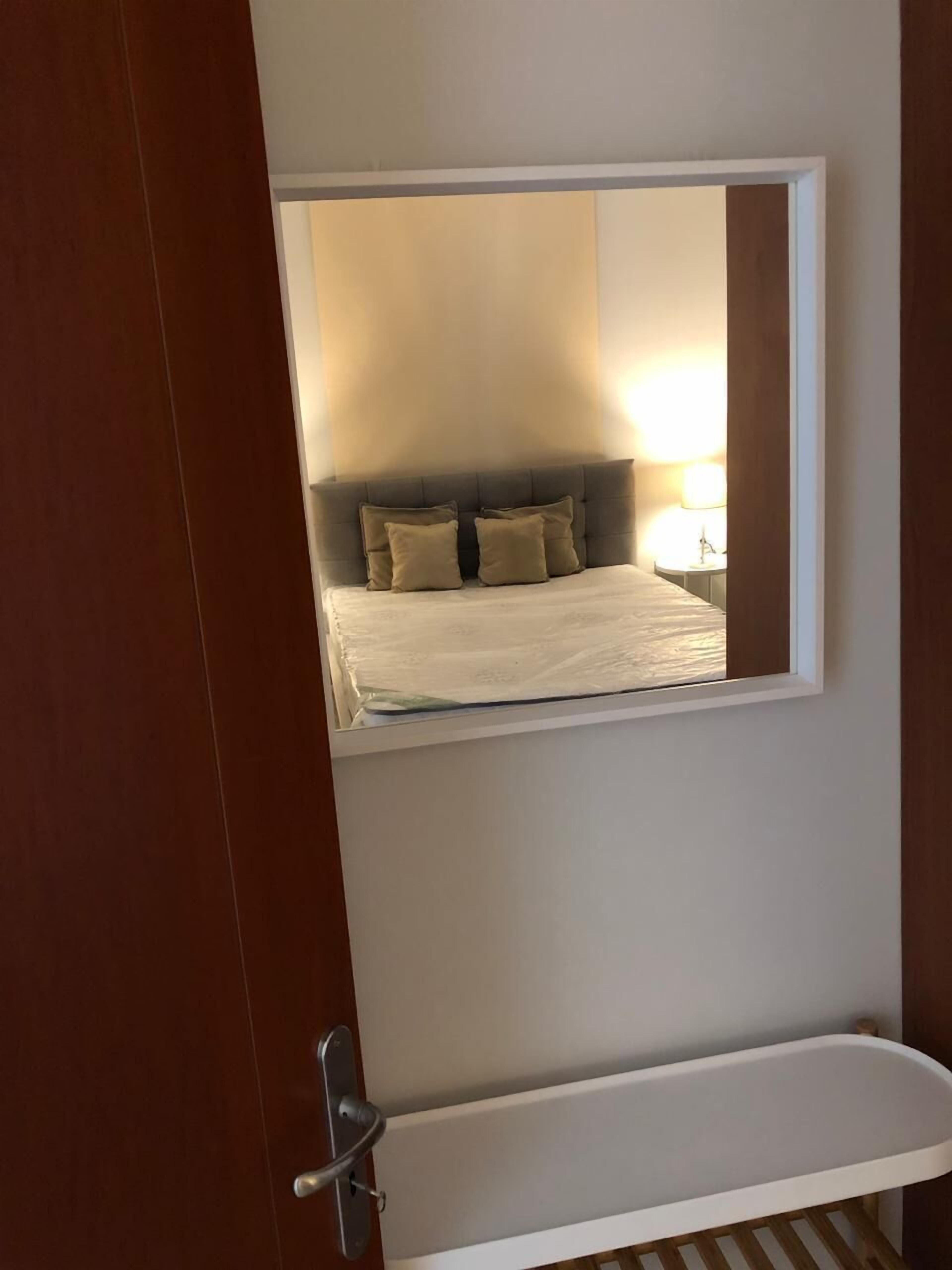 A bedroom with a large mirror reflecting a bed with beige bedding and pillows.