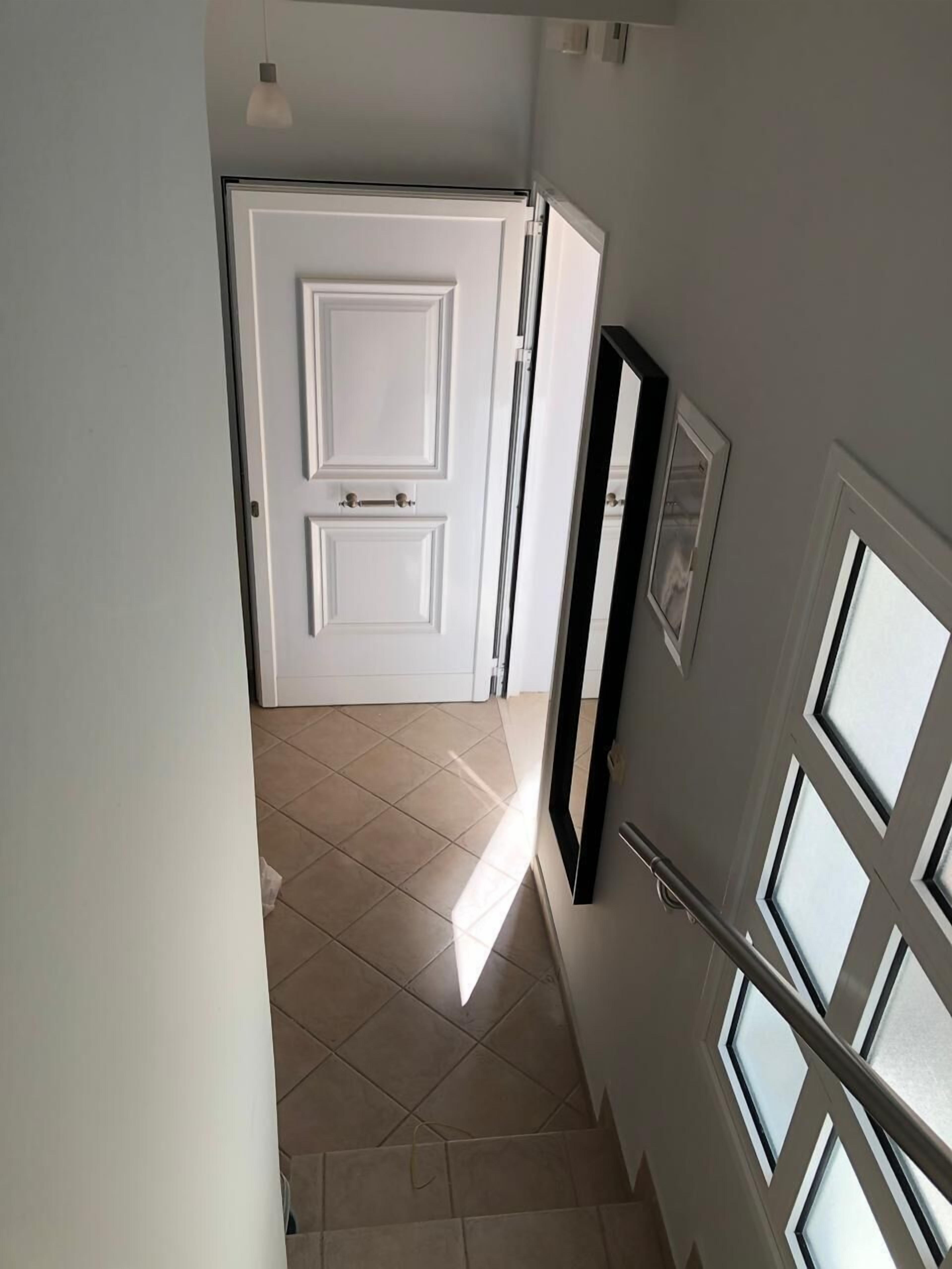 A hallway with a white door, a black-framed picture, and a window with a metal railing.
