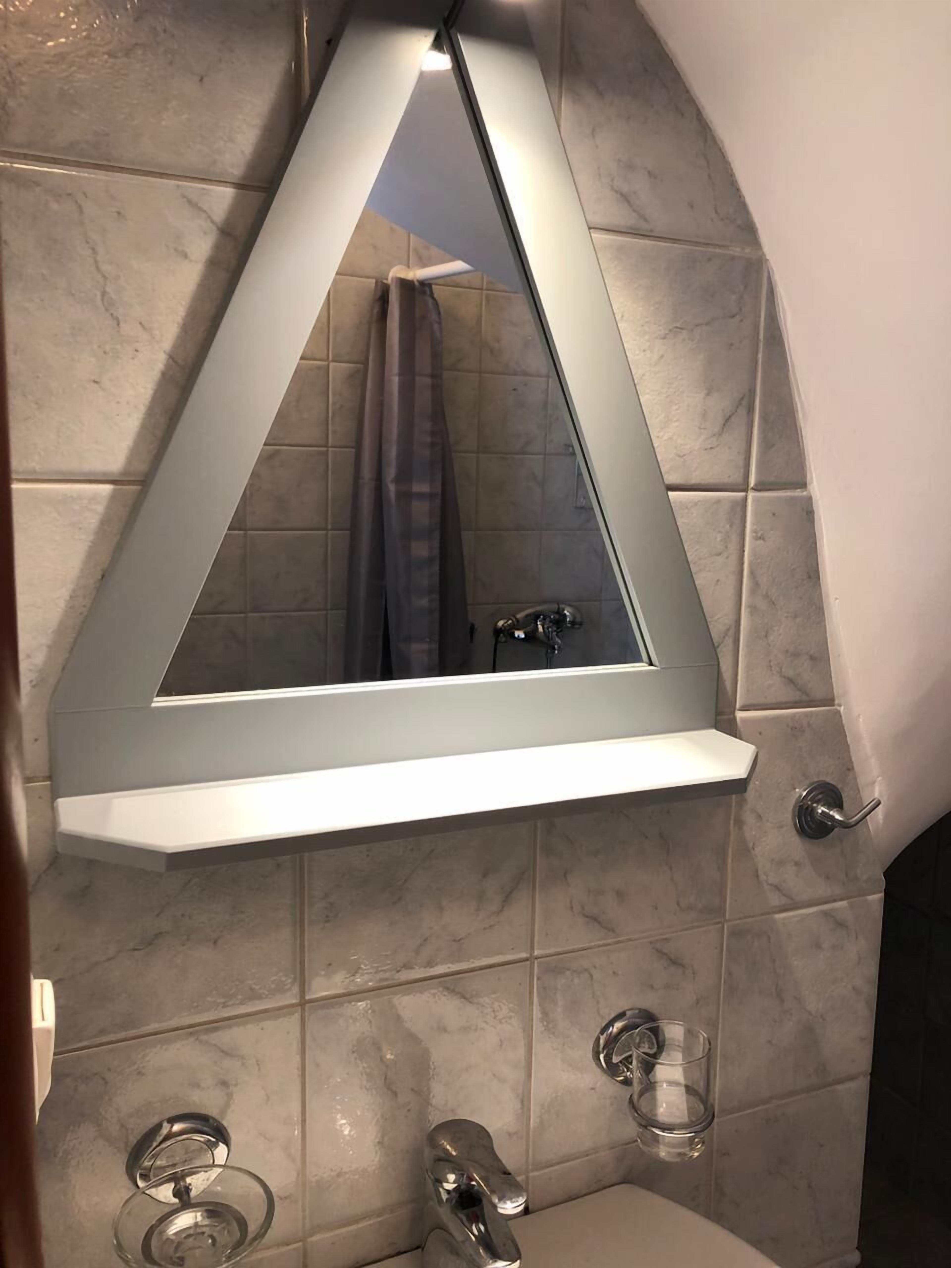 A bathroom with a triangular mirror, a sink, and a glass on the wall.