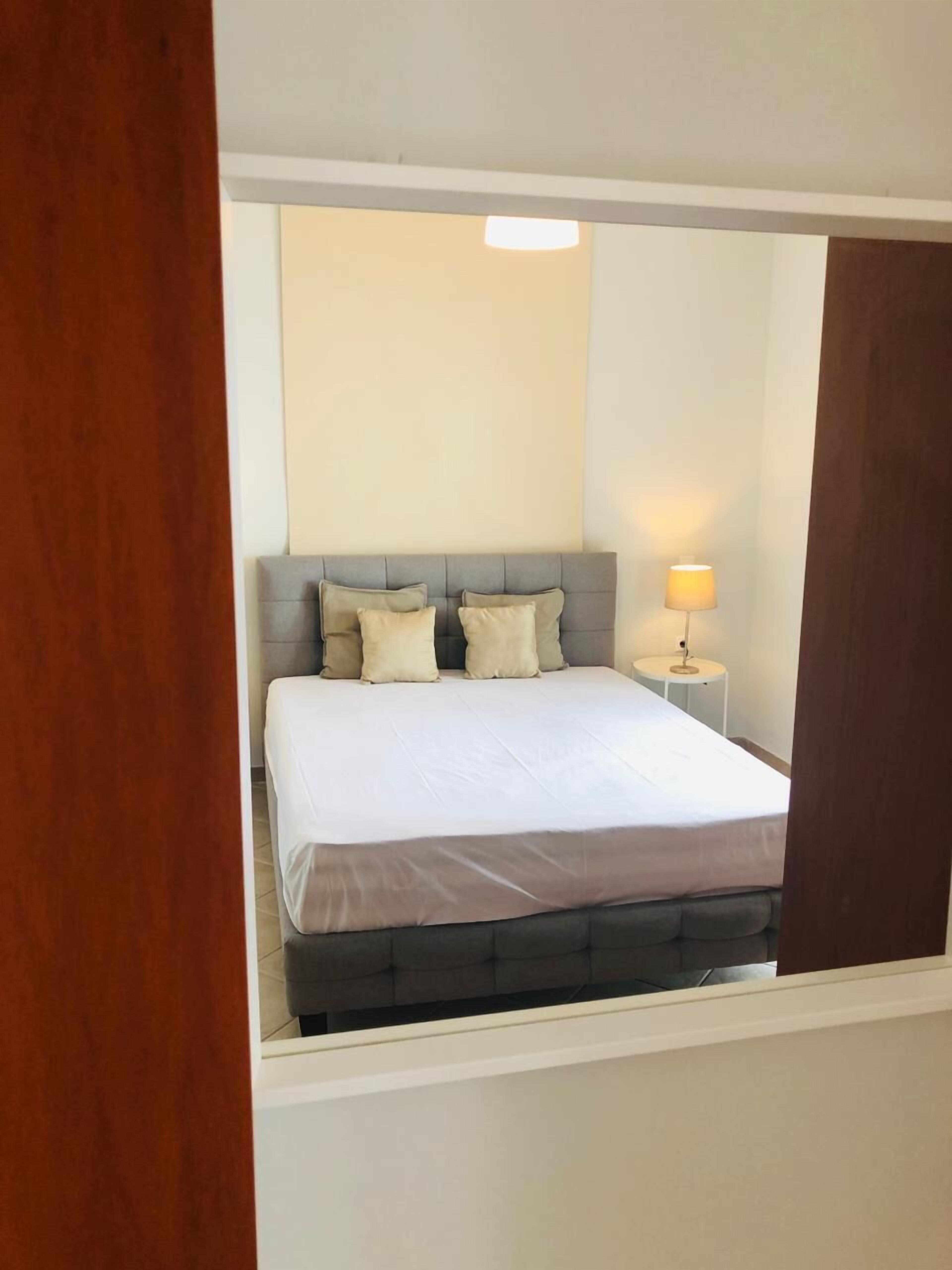 A bedroom with a bed, pillows, a bedside lamp, and a wooden door frame.
