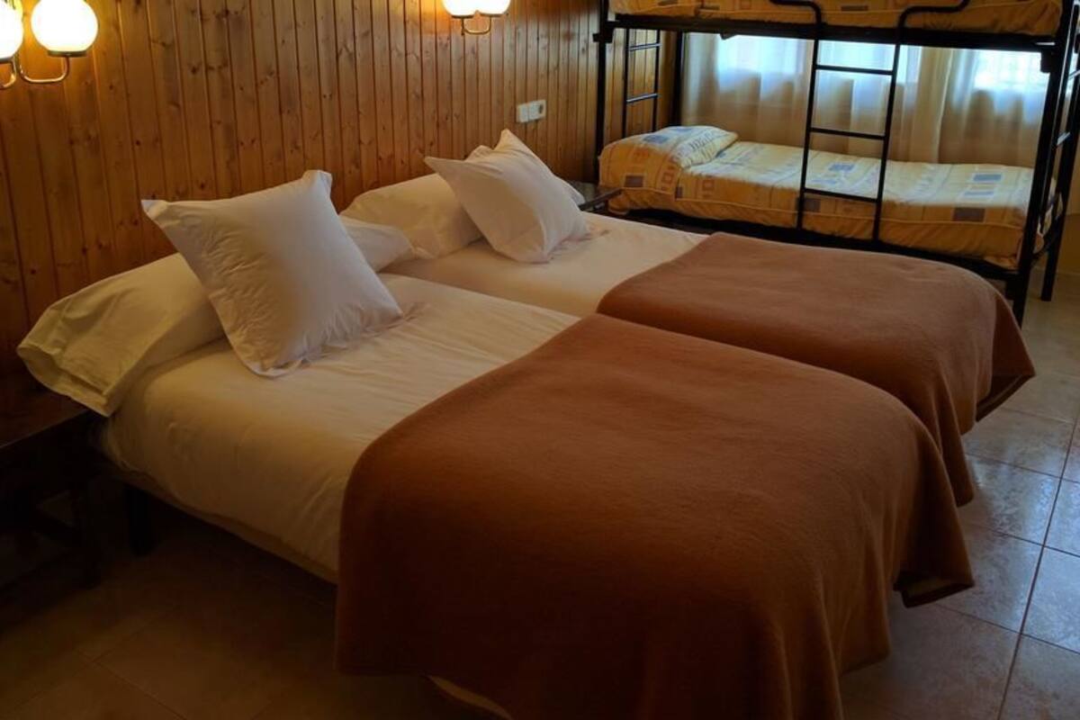 A room with two beds, wooden walls, and a bunk bed in the background.