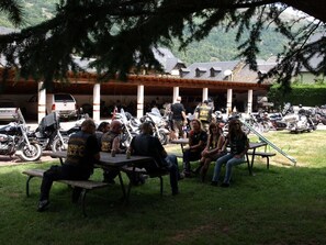 Un grupo de personas sentadas en mesas de picnic al aire libre, con motocicletas estacionadas al fondo.