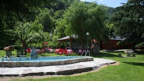 A pool area with stone steps, surrounded by green grass and trees. There are red and white tables and chairs, and a small pavilion in the background. - Hotel Talabart (Les)