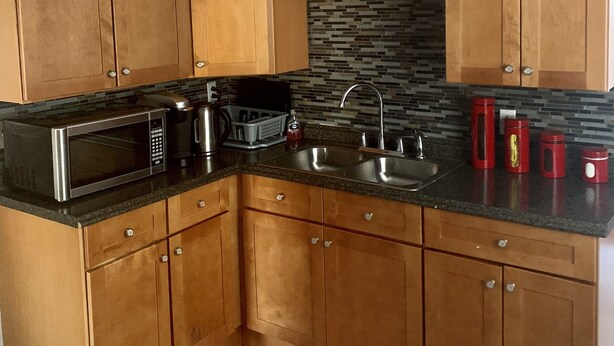 A kitchen with wooden cabinets, a black countertop, a microwave, a sink, and a ceiling fan. - 2BR-Free Parking, 5Min to Providence, 10Min to Ma-I-95 (Pawtucket)
