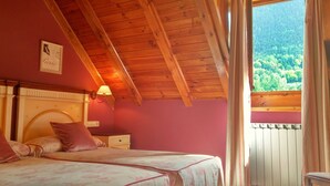 A bedroom with a wooden ceiling, a bed with floral bedding, a nightstand, a wall-mounted lamp, and a window with a view of a forest. - Hotel Colomers (Naut Aran)