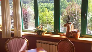 A dining area with a table and chairs, a window with a view of trees and a deer statue. - Hotel Colomers (Naut Aran)
