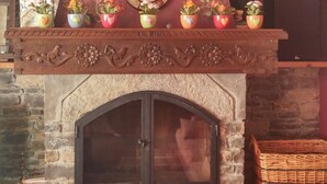 A stone fireplace with a mantel decorated with floral patterns and potted plants. - Hotel Colomers (Naut Aran)
