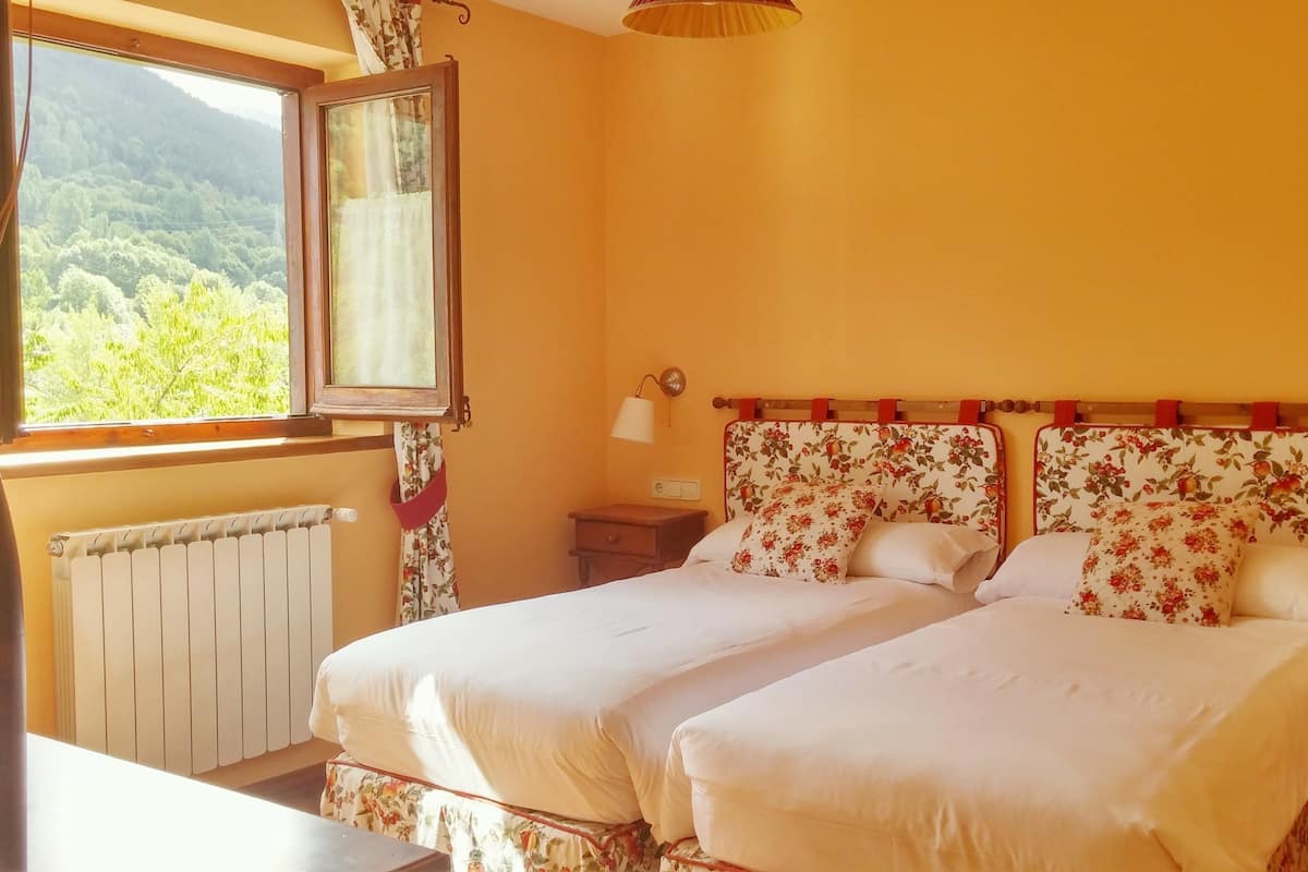 Een kamer met twee bedden, een raam met uitzicht op groen, een radiator en een nachtkastje.
