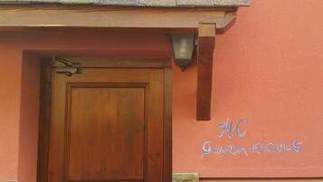 Una puerta de madera con un picaporte metálico, una pequeña ventana encima y una pared con el texto "AC GUARDAS ESQUIES" pintado en azul.
