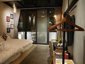 A bedroom with a bed, wooden floor, and a view through a glass door. - Grouppie Apartment (Hengchun)
