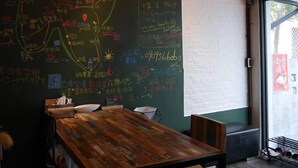 Ein Zimmer mit einem Holztisch und Stühlen, einer Wand mit Kreidetafel und Schrift sowie einem Fenster mit Blick.