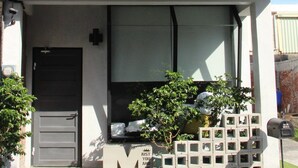 Ein moderner Gebäudeeingang mit einem großen 'M'-Schild, einem Briefkasten und einem kleinen Baum.