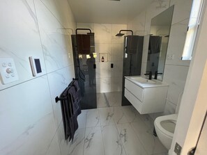 A modern bathroom with a white vanity, a large mirror, a toilet, and a towel rack. - Glenaire Apartments on Frazer St (Strahan)