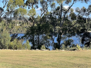 A grassy field with trees and a body of water in the background. - Glenaire Apartments on Frazer St (Strahan)