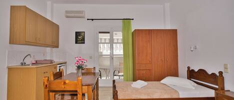 A bedroom with a wooden bed, a wooden desk, and a chair. There is a window with a green curtain and a view of a balcony.