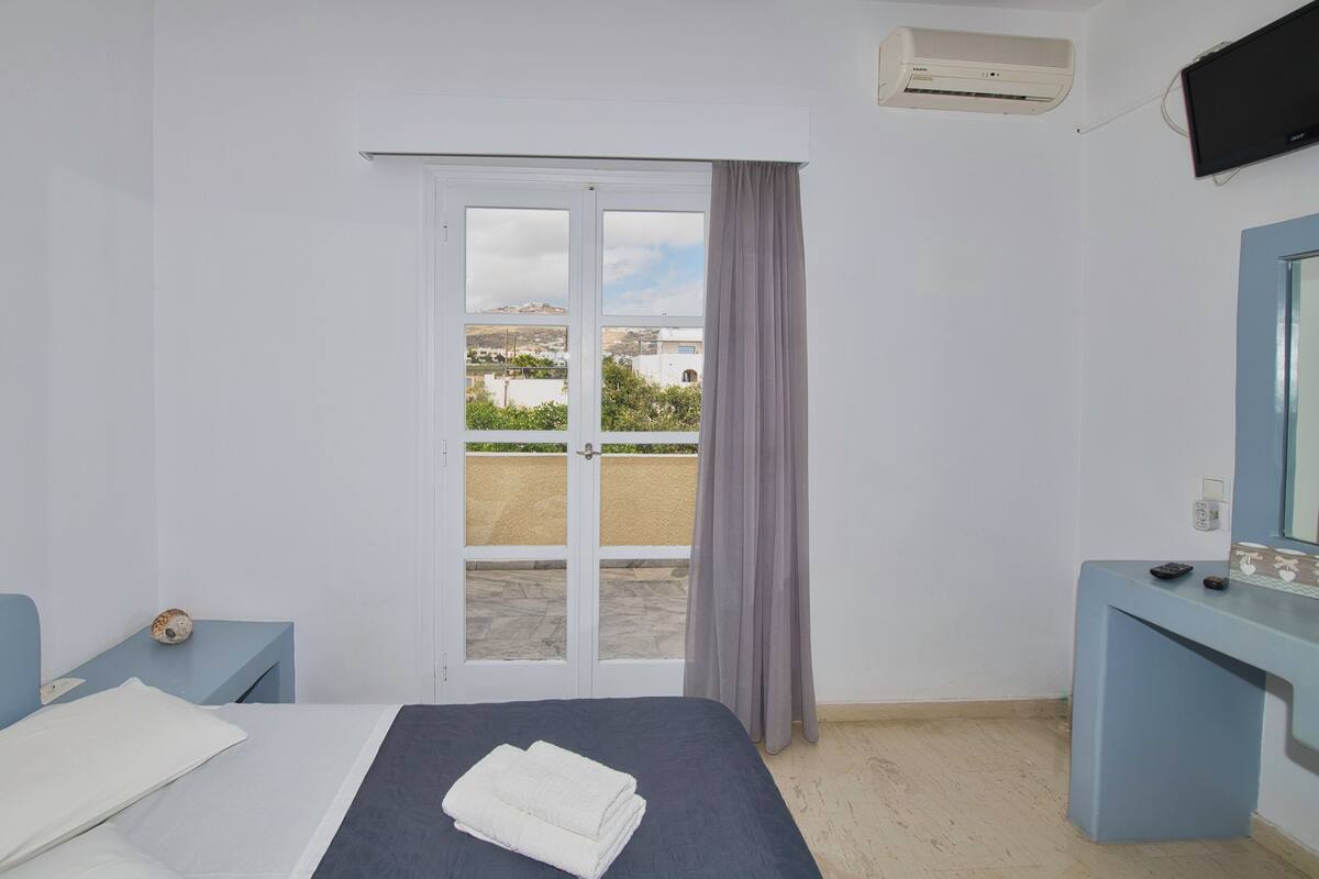 Une chambre d’hôtel équipée d’un lit, d’un bureau, d’un miroir, d’un appareil de climatisation et offrant une vue sur l’extérieur.