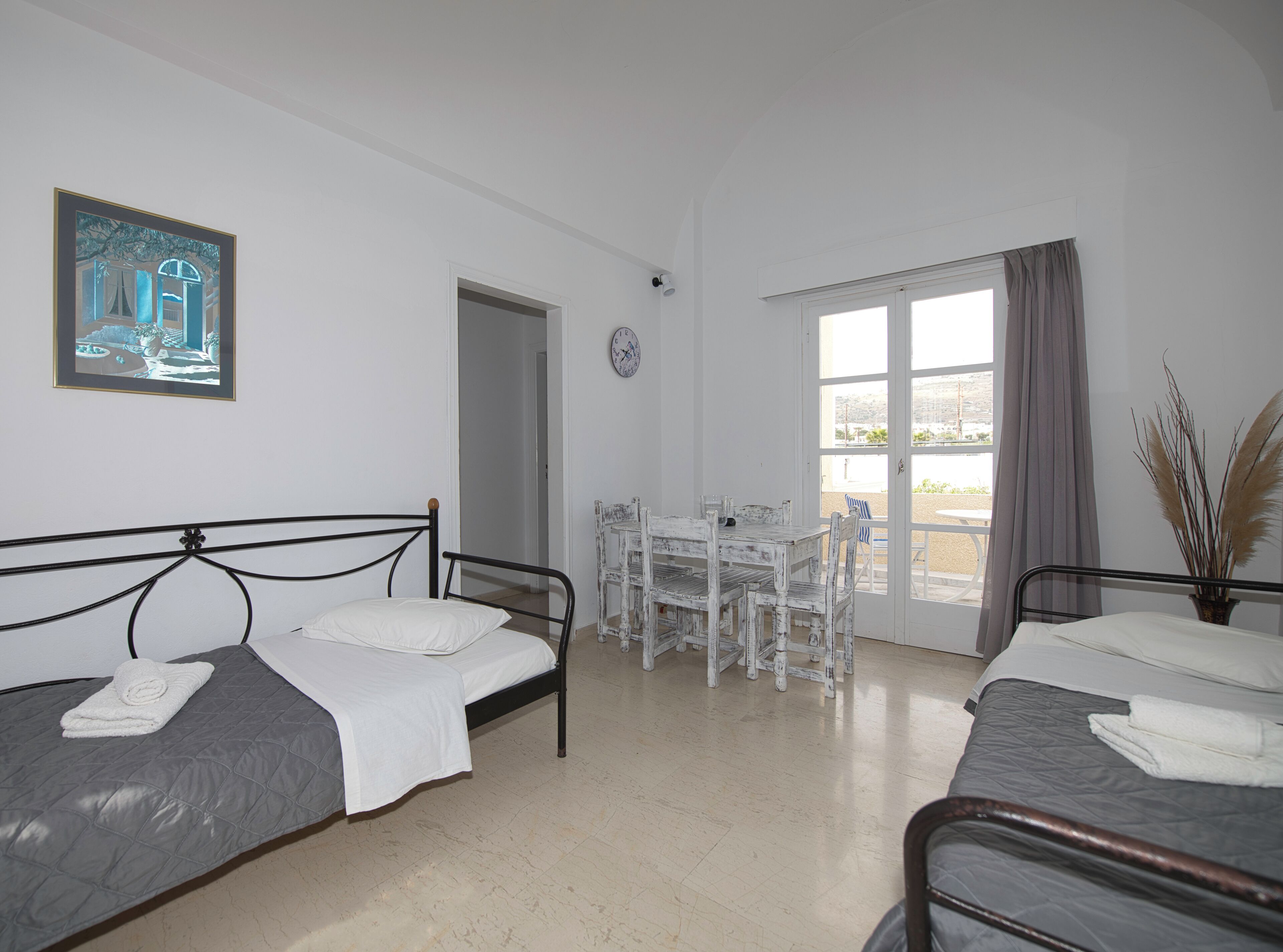 A room with two beds, a dining table with chairs, a window with curtains, and a painting on the wall.