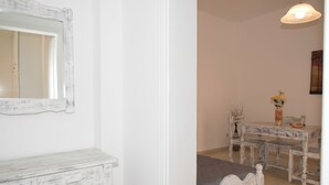 A room with a white dresser, a bed with a gray blanket, a rustic wooden table, and a hanging light fixture. - Ira Apartments (Santorini)