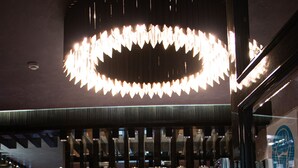 A hotel reception area with a modern design, featuring a reception desk, a large circular chandelier, and a sign indicating the hotel name and services.