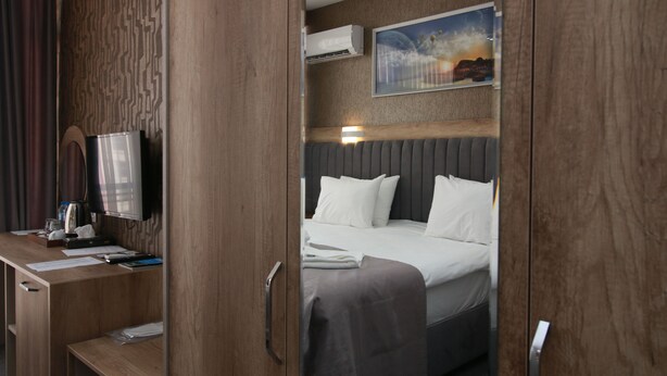 A hotel room with a wooden desk, a bed with white bedding, an air conditioning unit, and a framed picture on the wall.