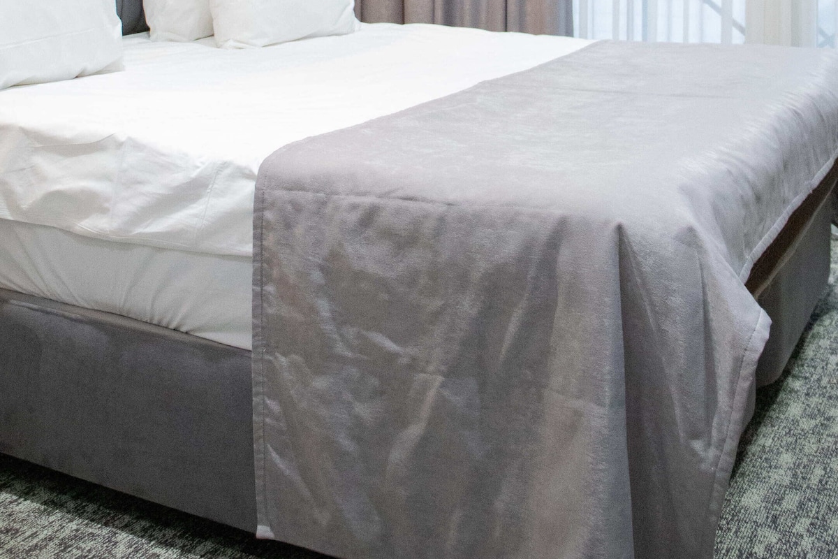 Een hotelkamer met een groot bed, een hoofdbord, een wandairconditioner en een raam met gordijnen.