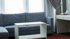 A modern hotel room with a grey sofa, a white coffee table, and a wooden desk.