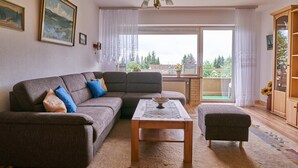 Een woonkamer met een modulaire bank, een salontafel en uitzicht op de buitenlucht door een groot raam.