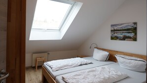 Een slaapkamer met dakraam, een bed met witte beddengoed, een houten hoofdbord, een nachtkastje en een radiator.