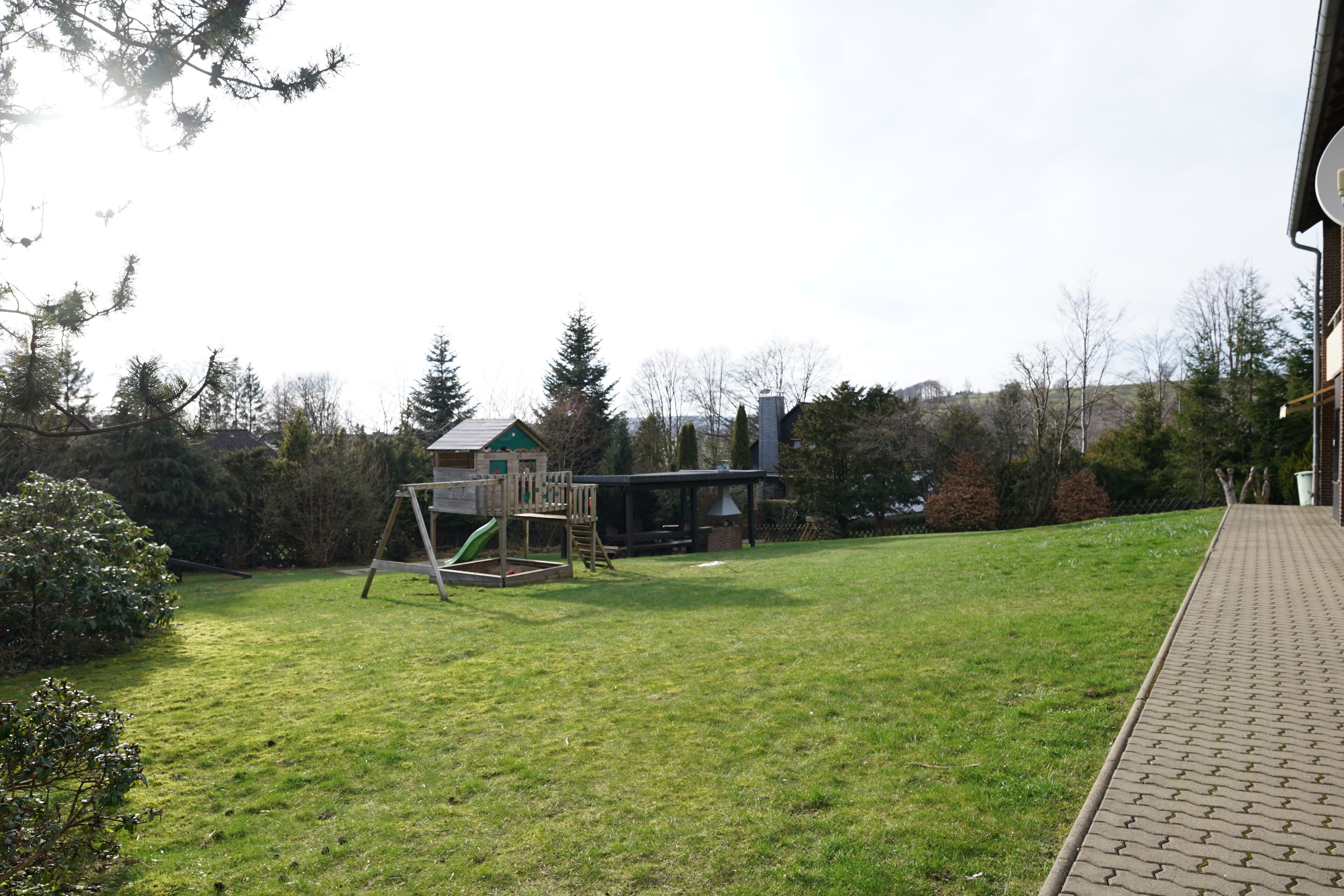 Une cour arrière verdoyante avec une aire de jeux et une maison en arrière-plan.