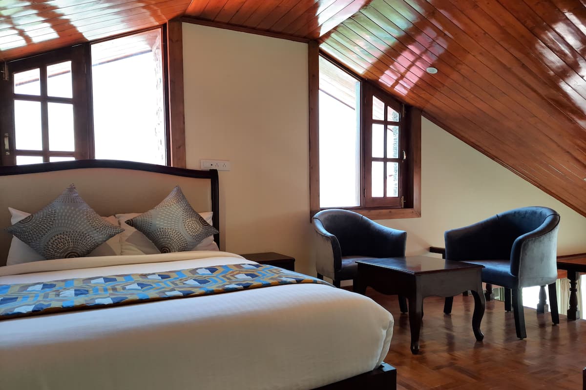 A bedroom with a large bed, two chairs, and a window.