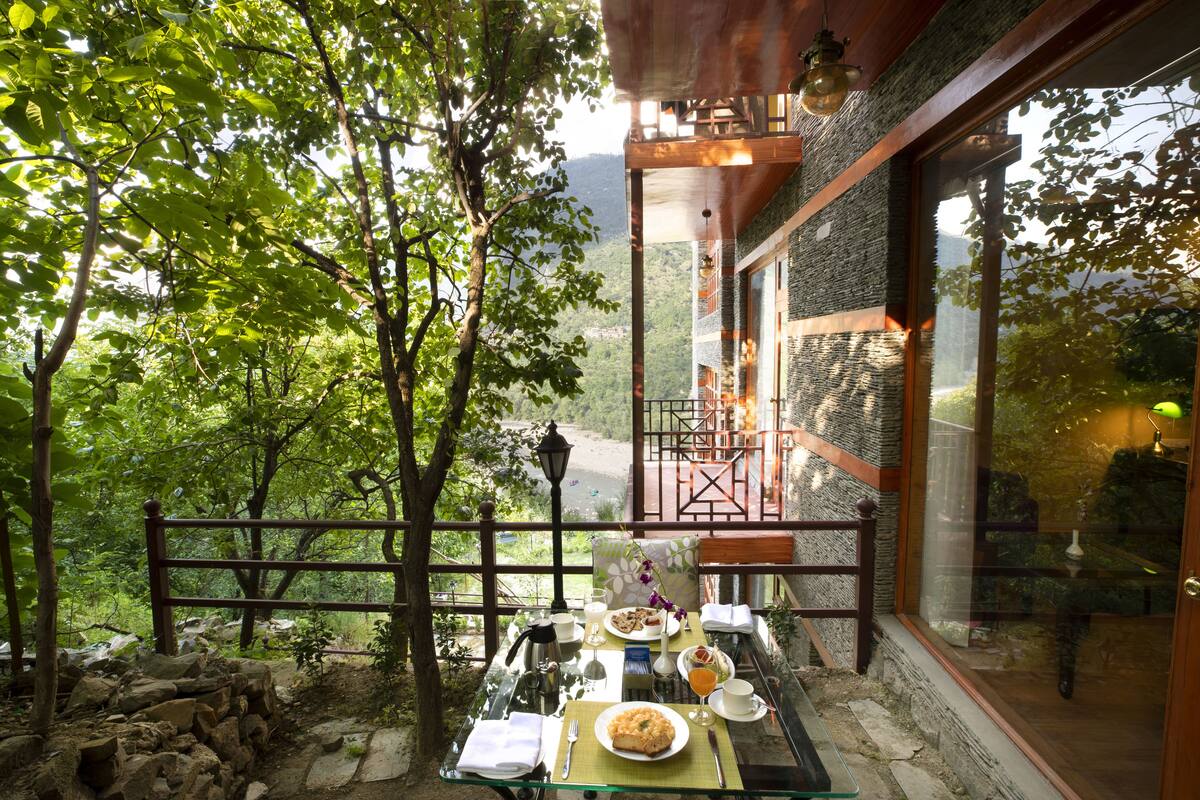 A dining table set outdoors with a scenic view, a stone wall, and a wooden deck.
