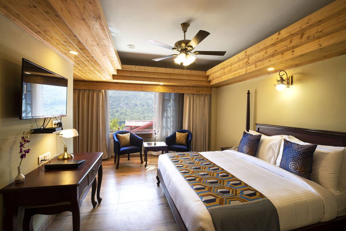 A hotel room with a bed, a desk, a chair, a ceiling fan, and a window with curtains.