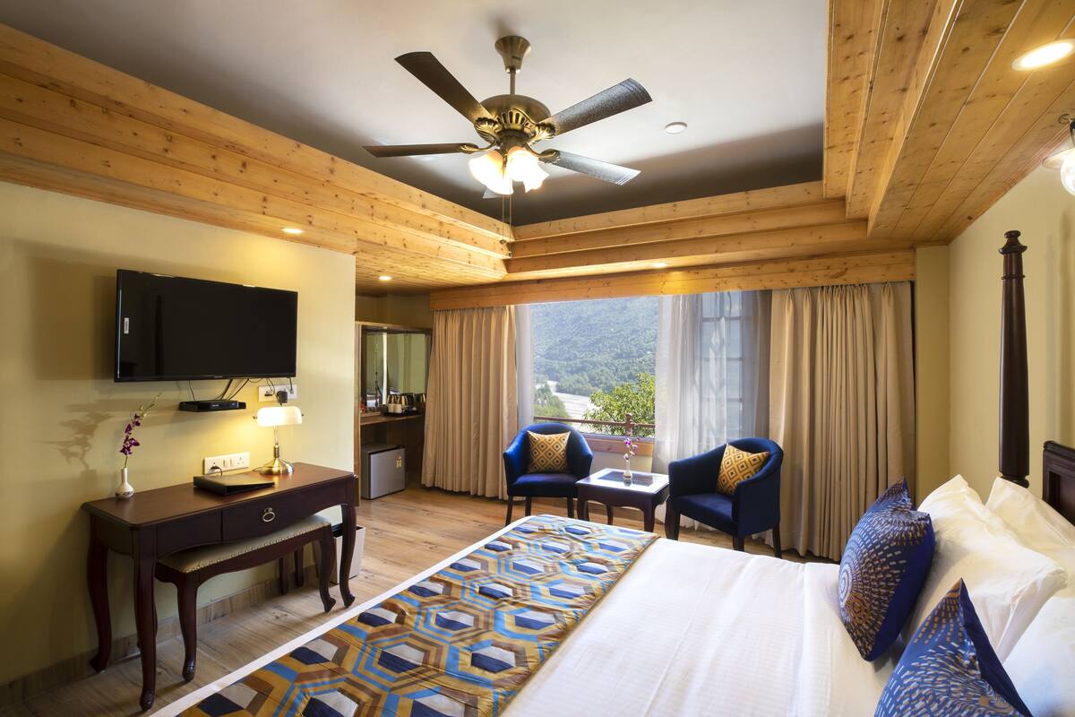 A hotel room with a bed, desk, chairs, a television, and a view of the outdoors.