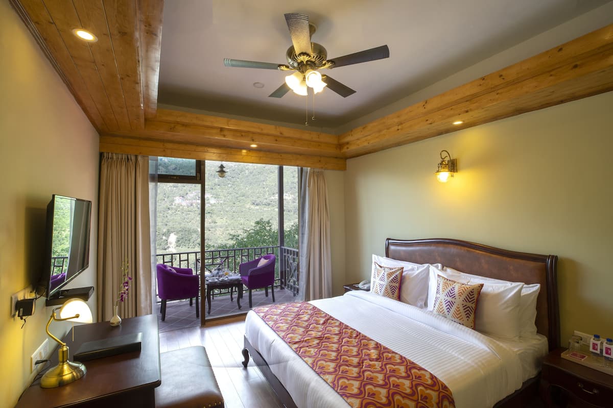 A hotel room with a bed, a desk with a lamp, a chair, a television, and a balcony with a chair.