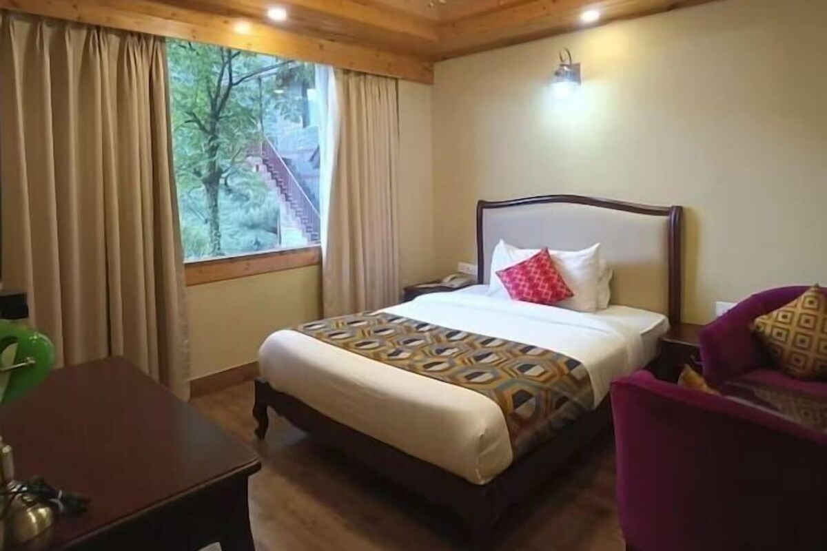 Une chambre d’hôtel avec un lit, une chaise, un bureau et une fenêtre avec des rideaux.