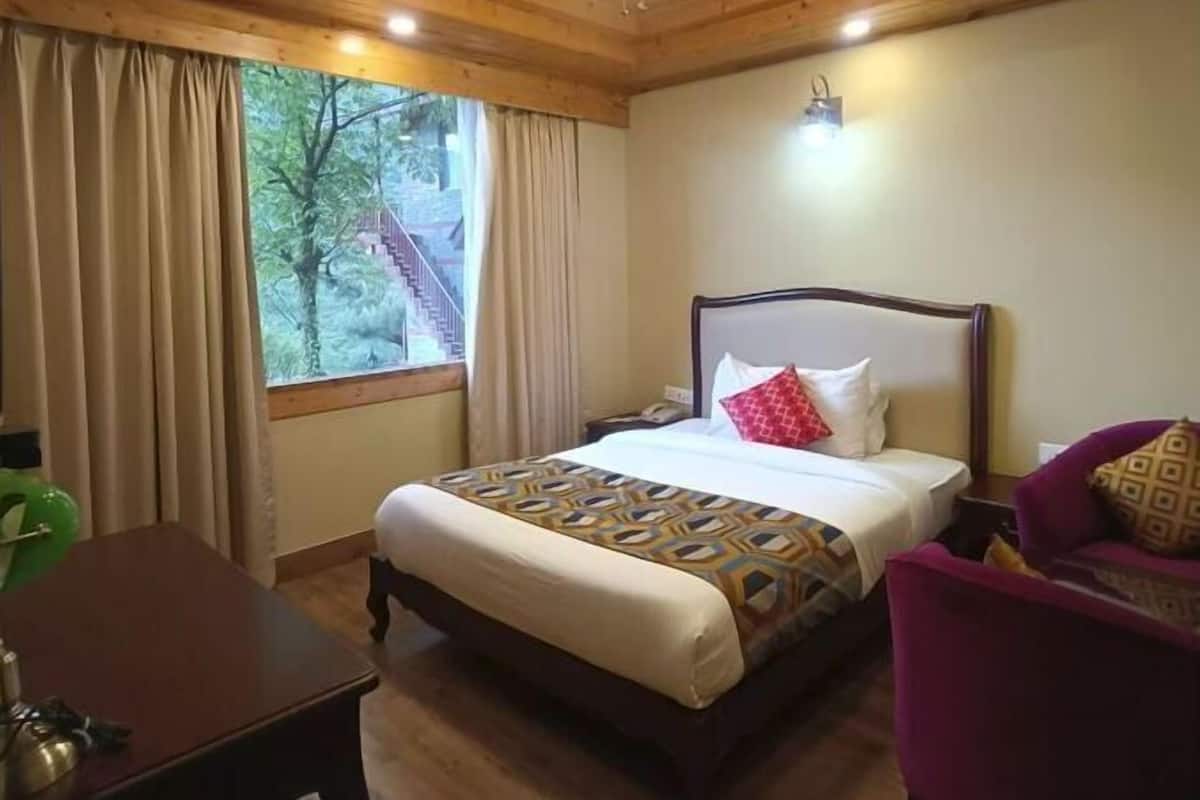 A hotel room with a wooden ceiling, a bed with patterned bedding, a desk, and a chair.