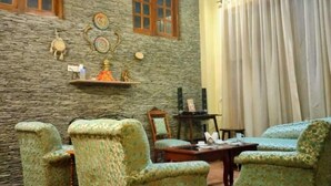 A room with a stone wall, wooden beams, a chandelier, and patterned armchairs. - Regenta Inn By Riverside Manali (Kullu)