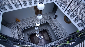 A high-angle view of a modern atrium with geometric patterned flooring, a central seating area, and hanging light fixtures. - Cevik Palace Otel (Antalya)
