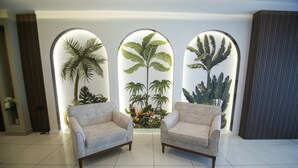 A room with two beige armchairs, a white tiled floor, and three arched windows displaying tropical plants. - Cevik Palace Otel (Antalya)