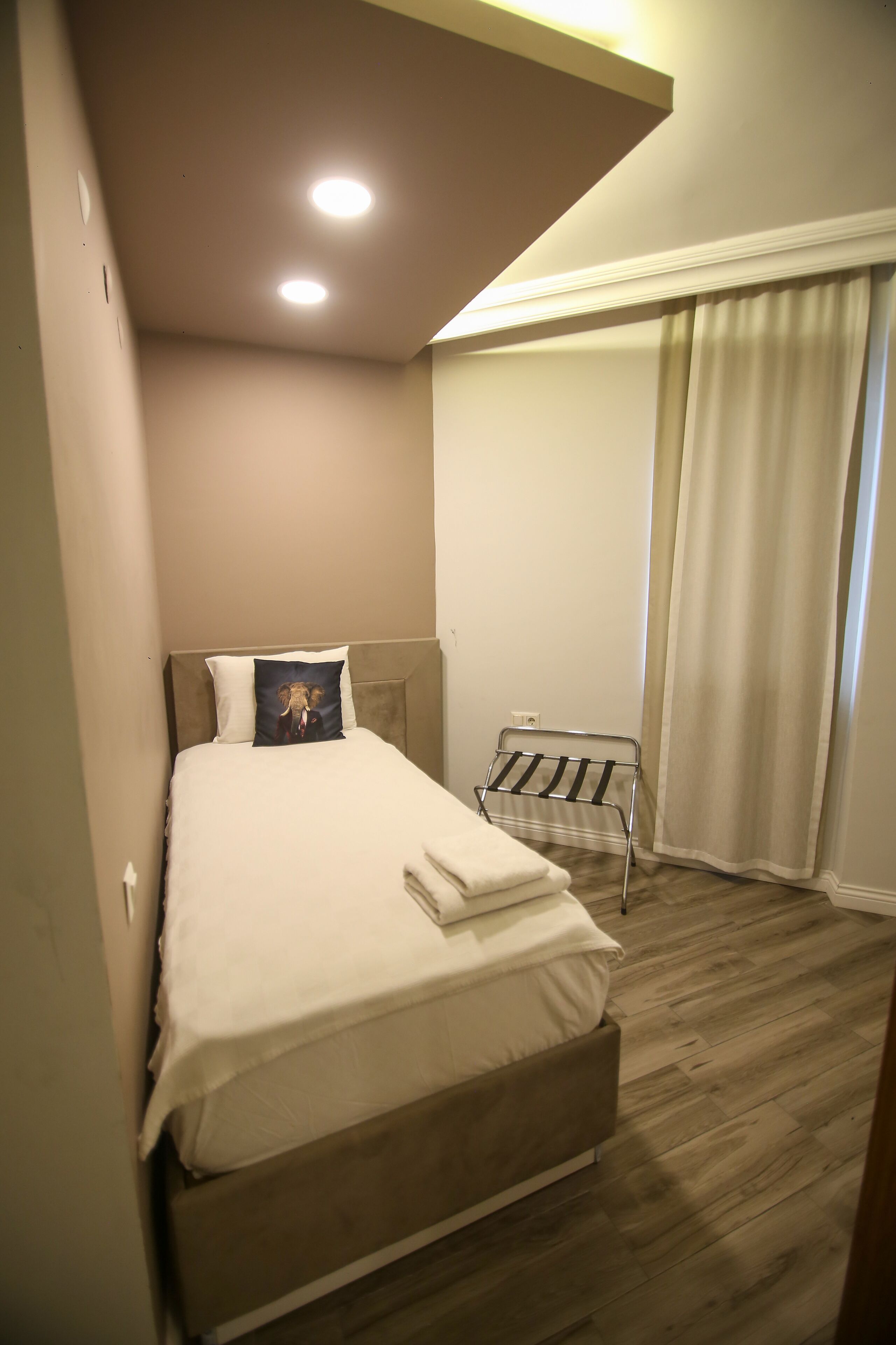 A neatly made bed with a pillow, a small table with a towel, and a window with curtains.