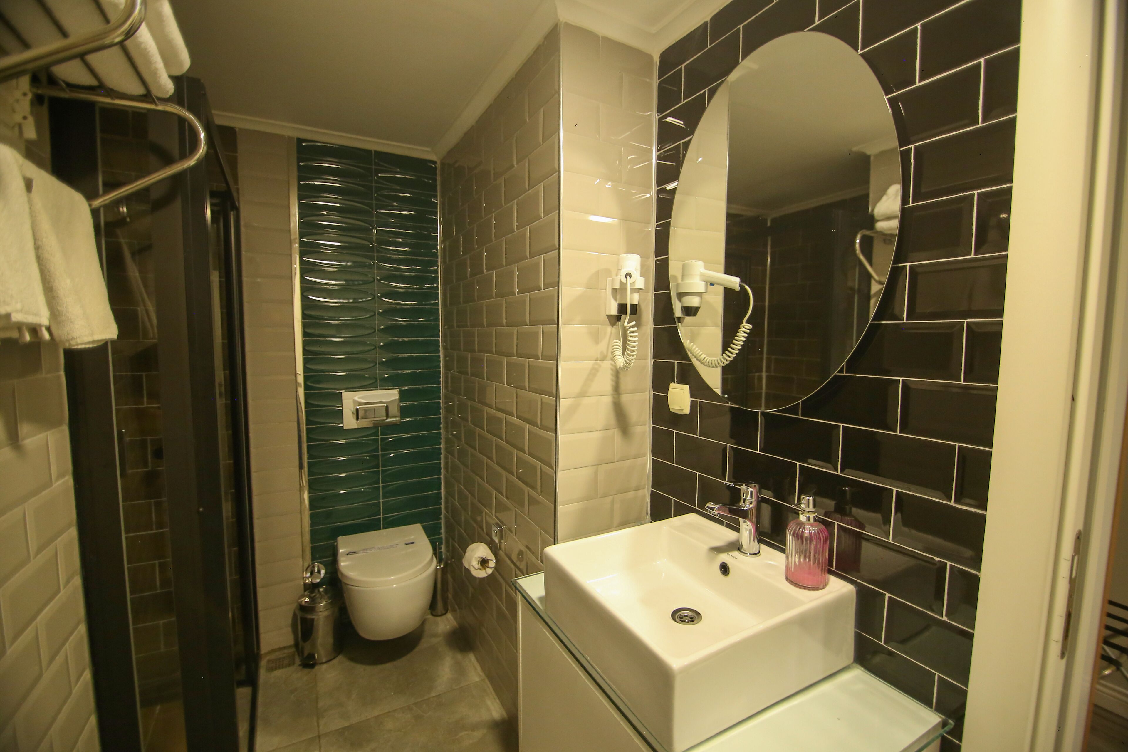 A bathroom with a glass sink, a mirror, a hairdryer, and a toilet.