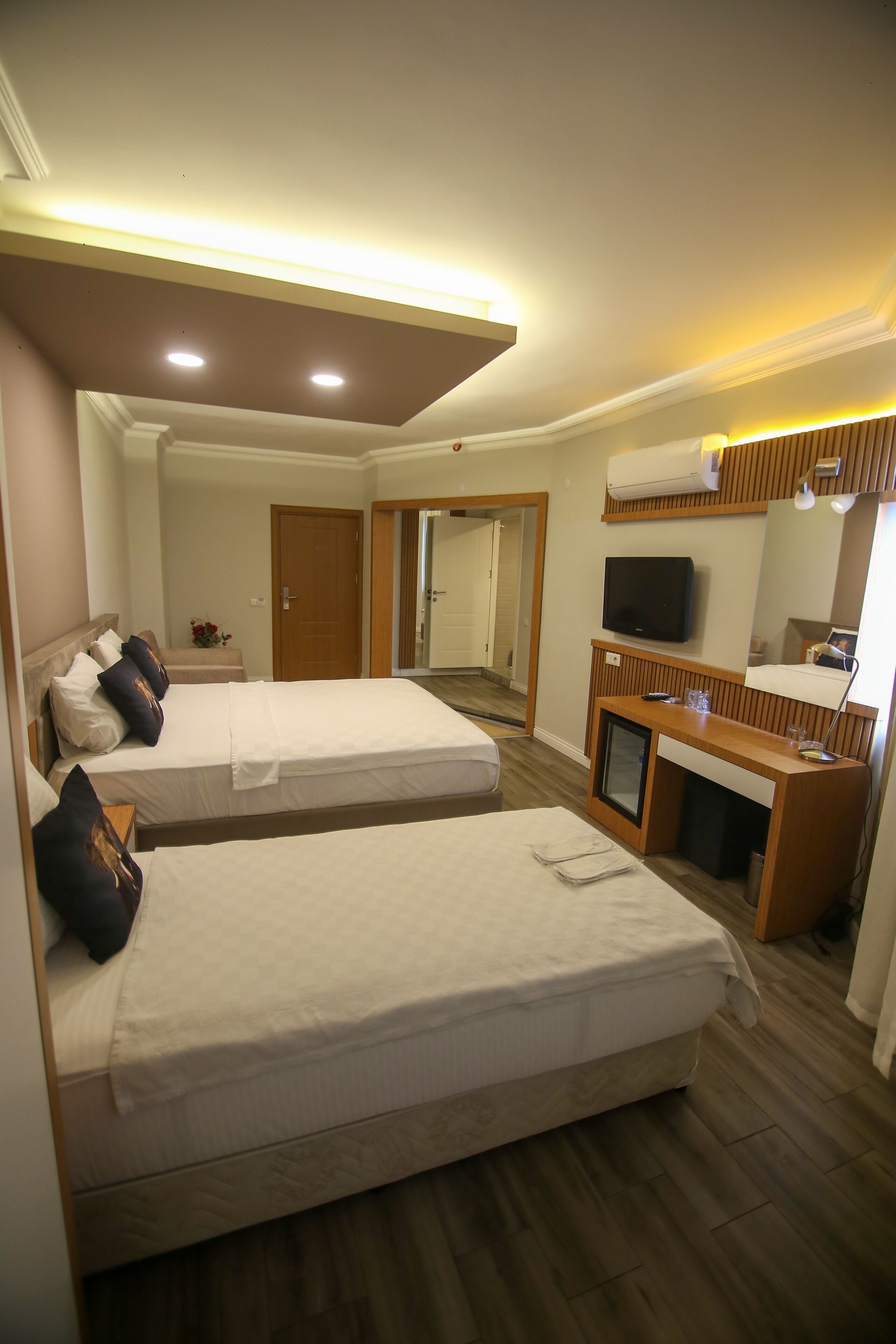 A hotel room with two beds, a TV, a desk with a computer, and a mirror.