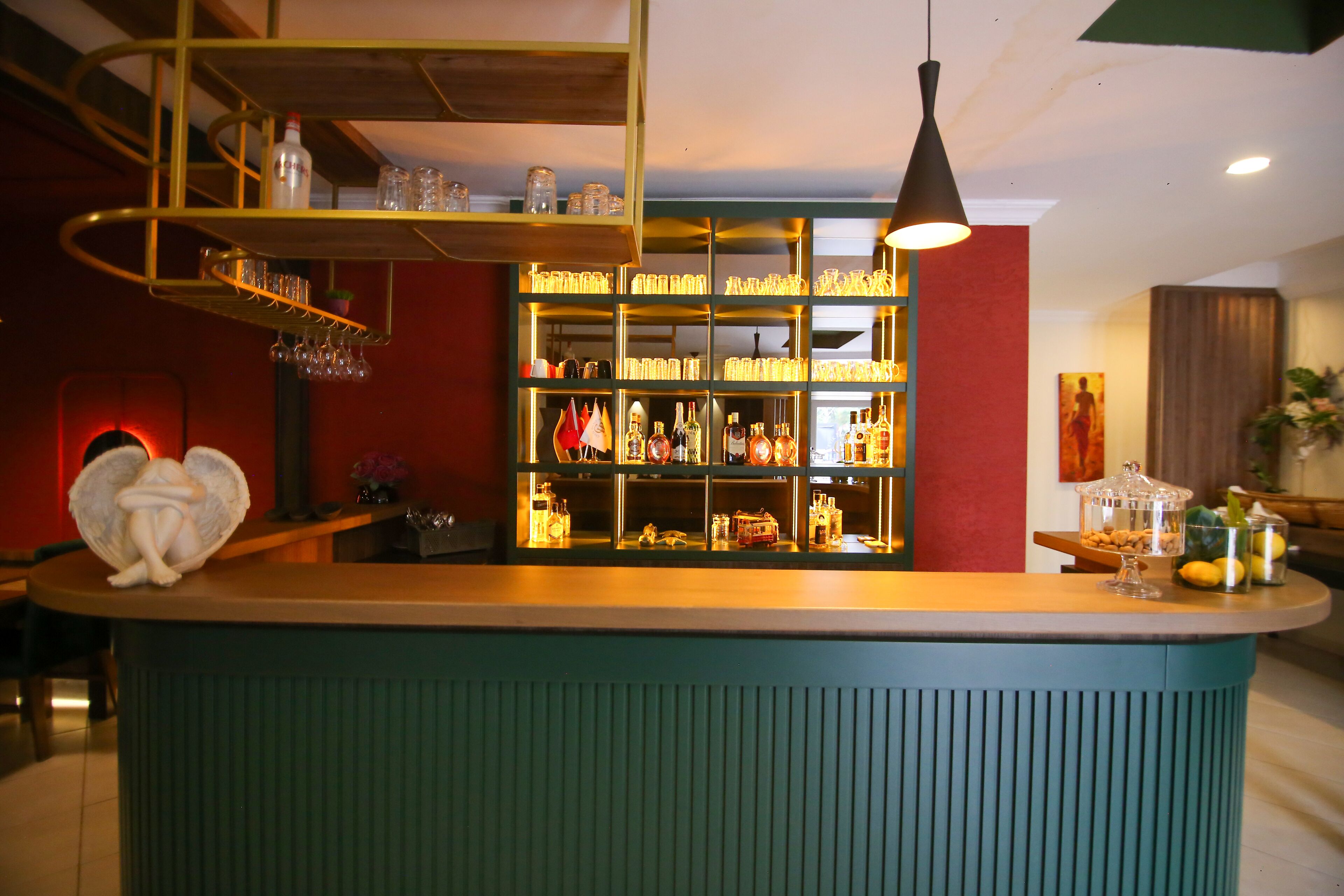 Eine Bar mit Regalen voller Flaschen und Gläsern, einer dekorativen Engelsfigur und einer Pendelleuchte.