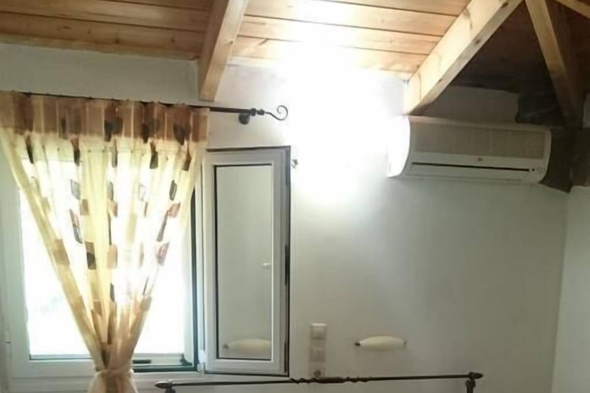 A bedroom with a bed, a bedside table, a nightstand, a mirror, and a window with curtains.