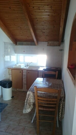A compact kitchen with a wooden ceiling, a tiled backsplash, a sink, and a dining table with chairs.