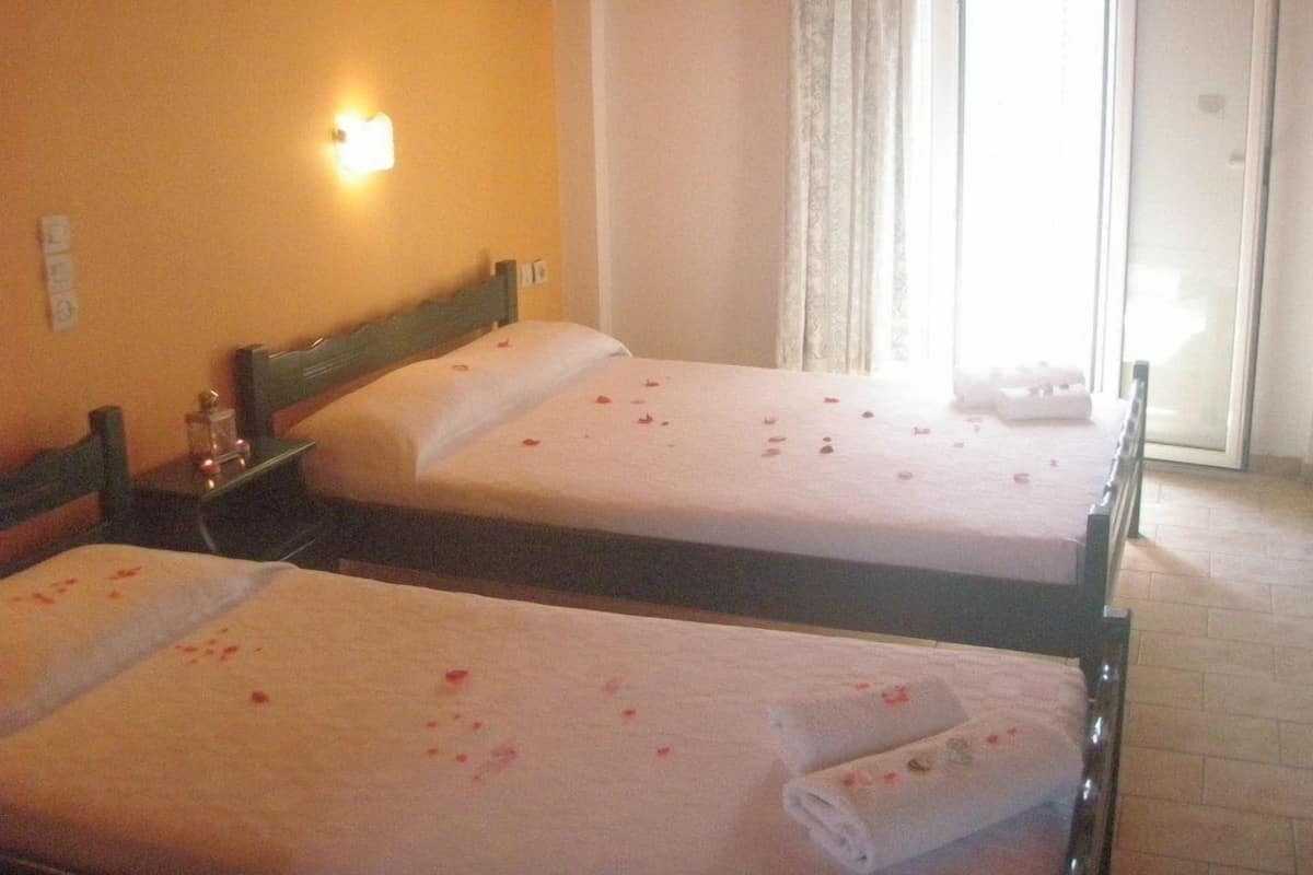 A hotel room with two beds, a nightstand, a lamp, and a view of the outside through a window.