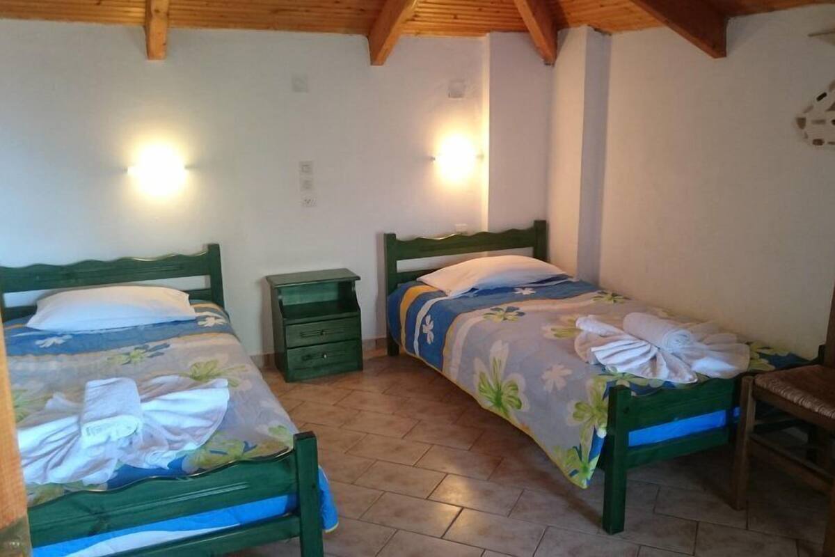 A bedroom with two single beds, a nightstand, a chair, and a wall-mounted light fixture.