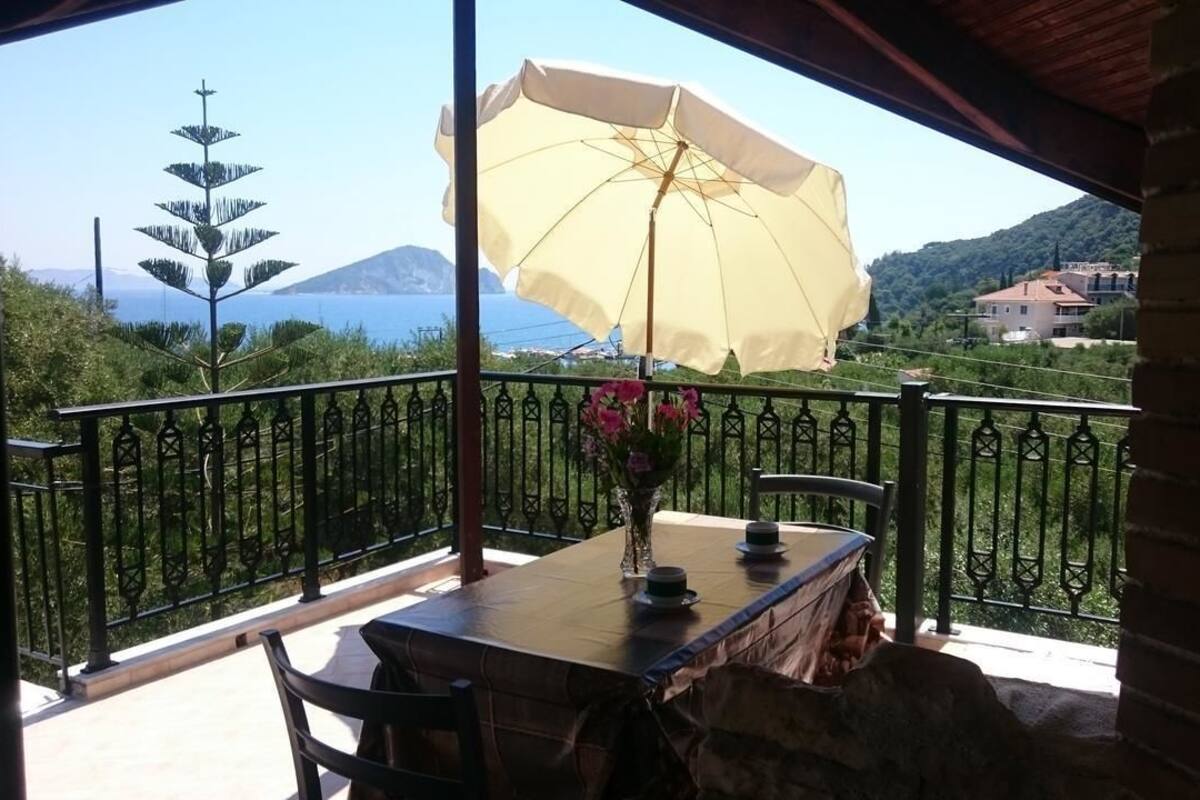 A balcony with a table, chairs, a yellow umbrella, and a vase of flowers.