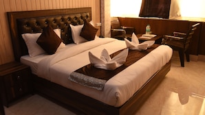 A neatly made bed with a decorative headboard, a bedside table with a lamp, and a chair near the window. - HBC Hotel Accurate (Rishikesh)