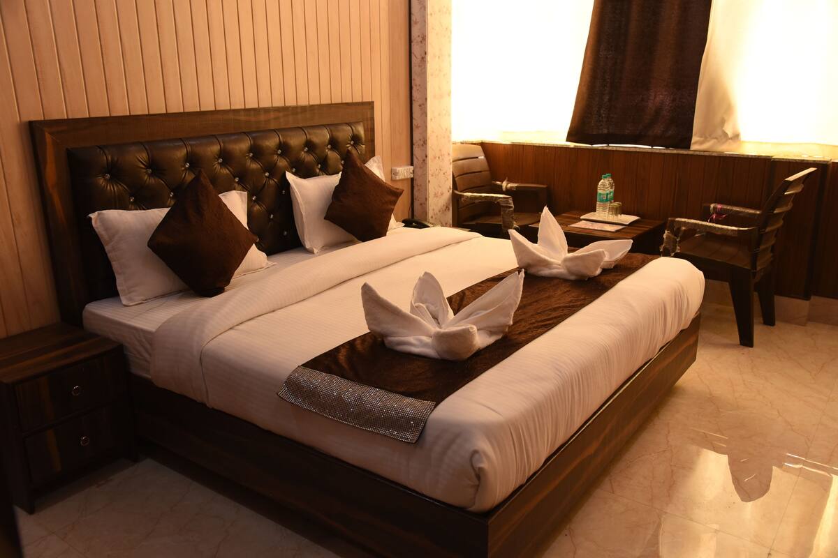 A neatly made bed with a decorative headboard, a bedside table with a lamp, and a chair near the window.